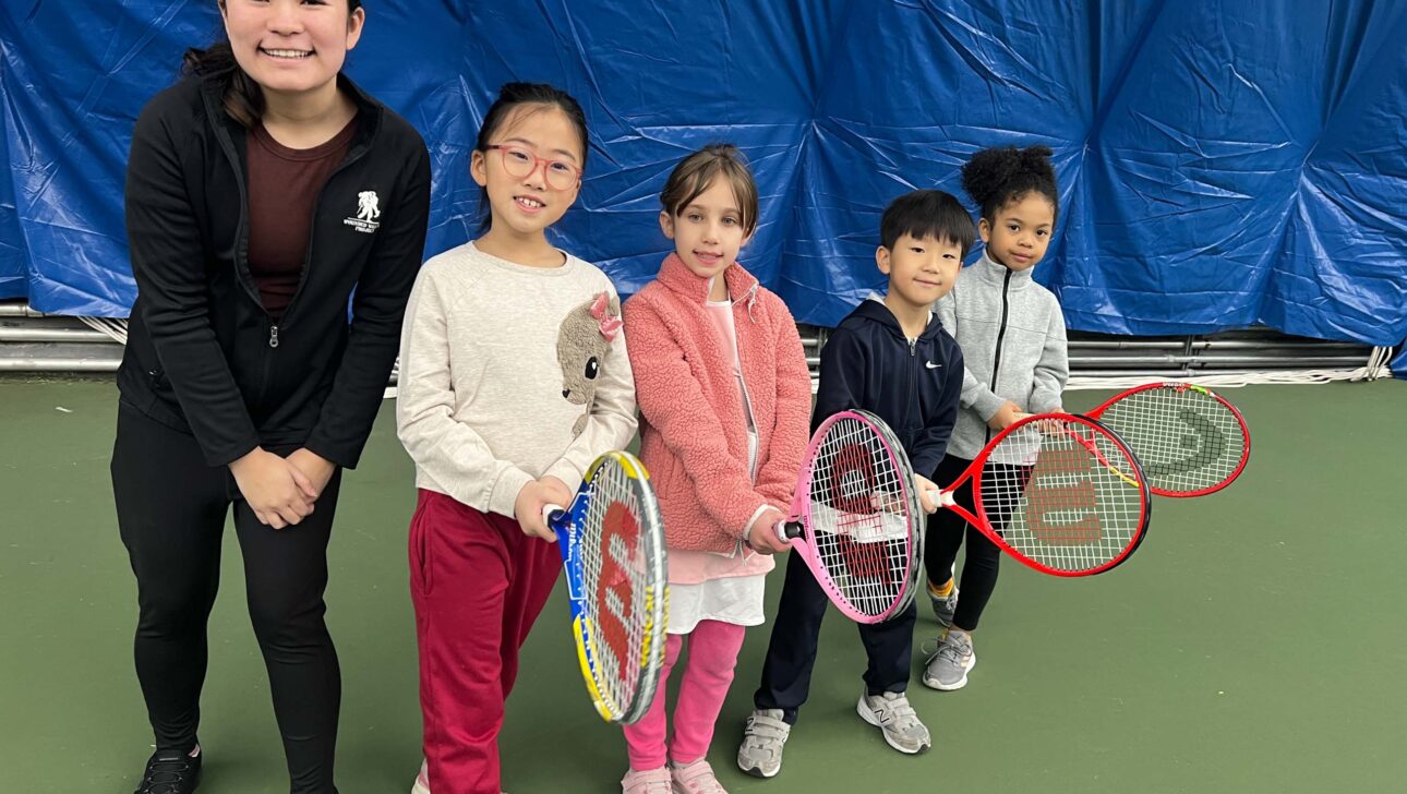 A group of children holding tennis rackets on a tennis court.