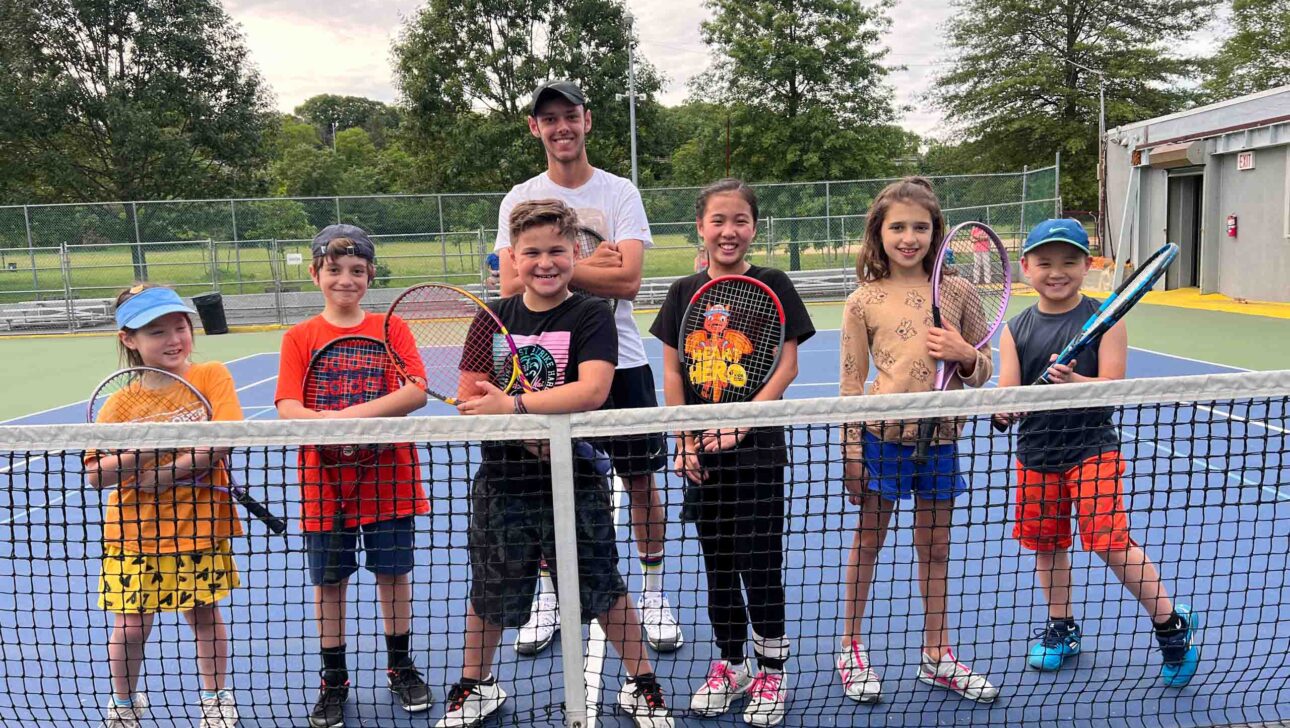 A group of kids posing for a picture on a tennis court.