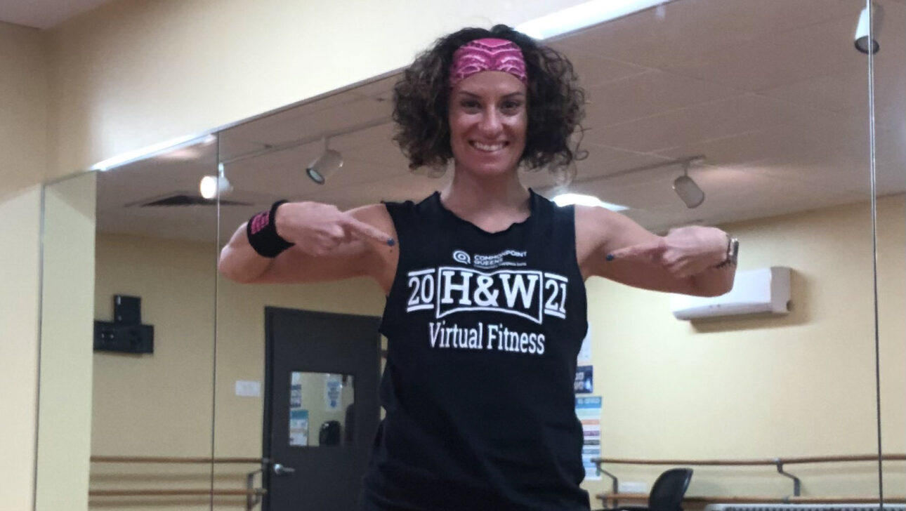 A woman in a black tank top and pink leggings posing in a dance studio.