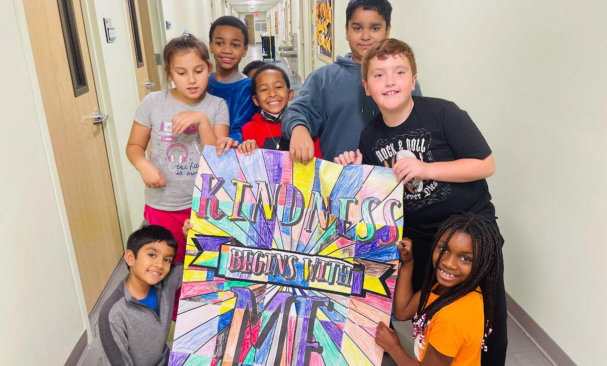 A group of kids posing with a sign in a hallway.