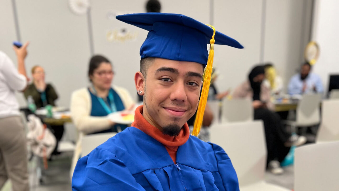 A man in a blue graduation gown sitting on a chair.