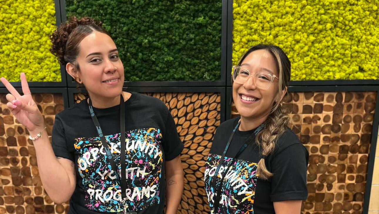 Two women in t - shirts standing in front of a green wall.