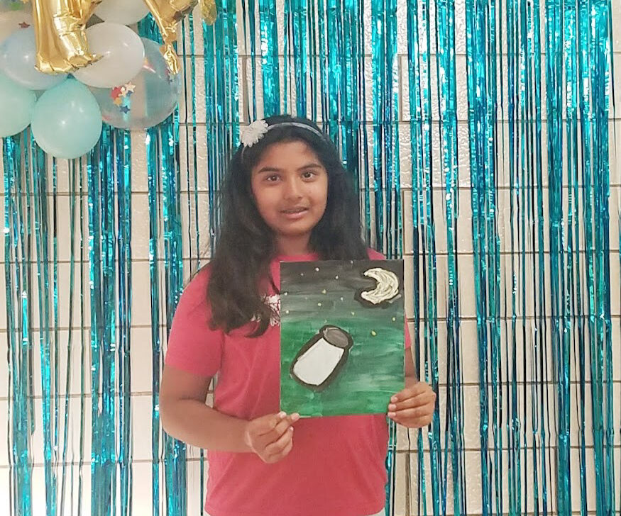 At BELL Academy, a girl holds a penguin painting while standing in front of colorful balloons.