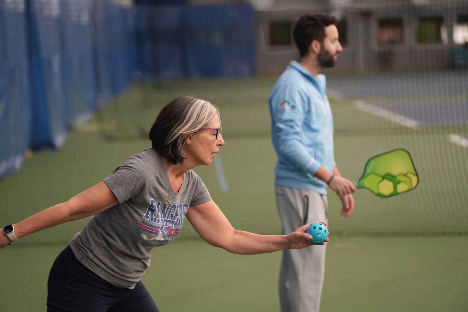 A woman prepares to serve a pickleball on an indoor court, standing next to a man holding a paddle.