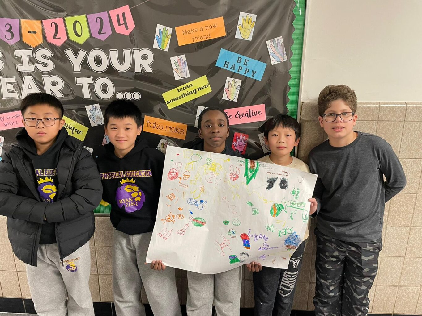 A group of MS 216 students standing in front of a bulletin board.