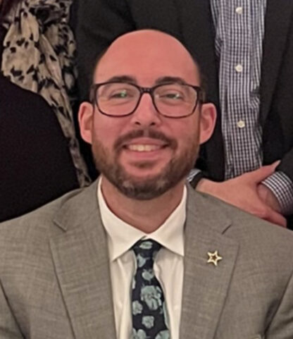 Jared Mintz, a man in a suit and tie, smiles in front of a group of people.