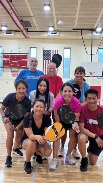 A group of adults posing for a picture with table tennis rackets at Little Neck.
