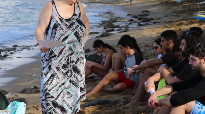 A woman is standing on the beach with a group of people, enjoying the beautiful scenery.