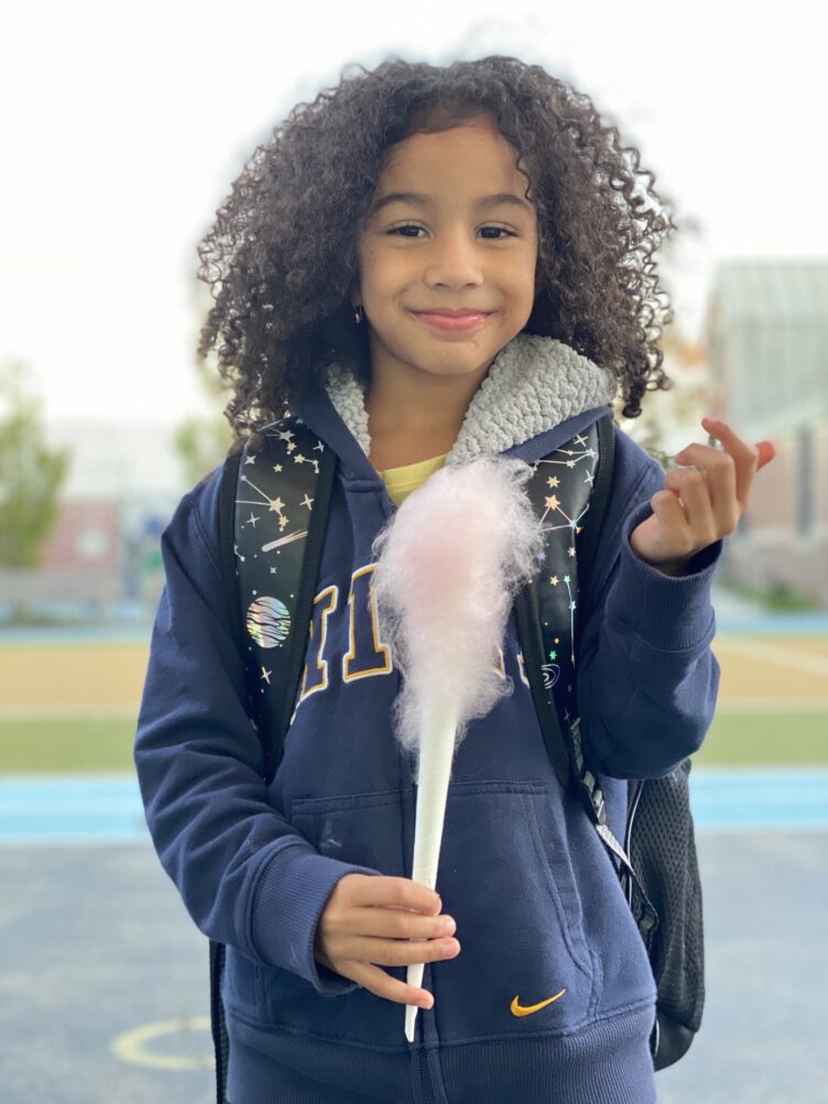 A young girl with curly hair holding a cotton candy at PS 50.
