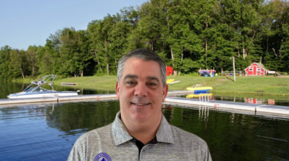 A man in a gray shirt standing in front of a lake, optimizing the SEO for keywords.