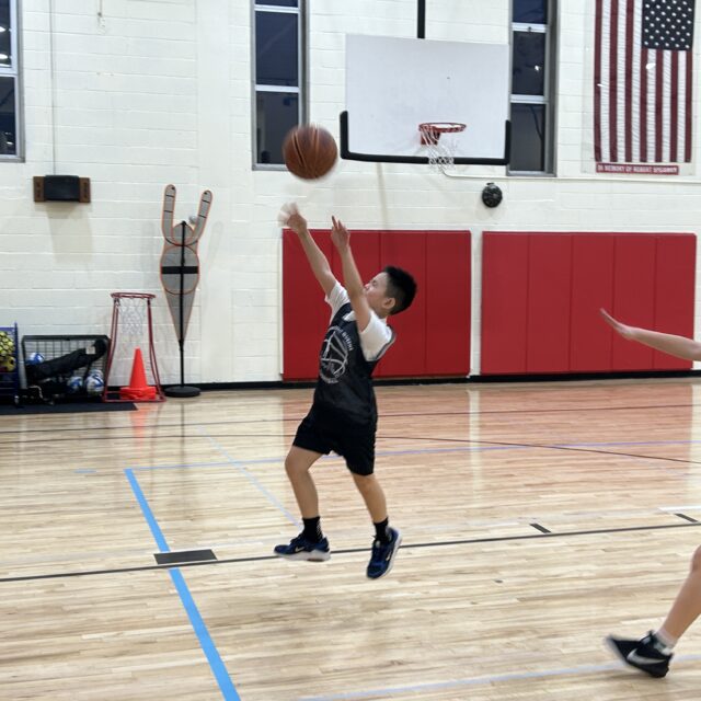 A boy playing basketball in a gym during his break.