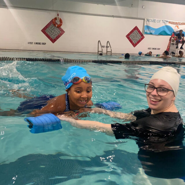A young girl in a swimming pool with an aquatics teacher.