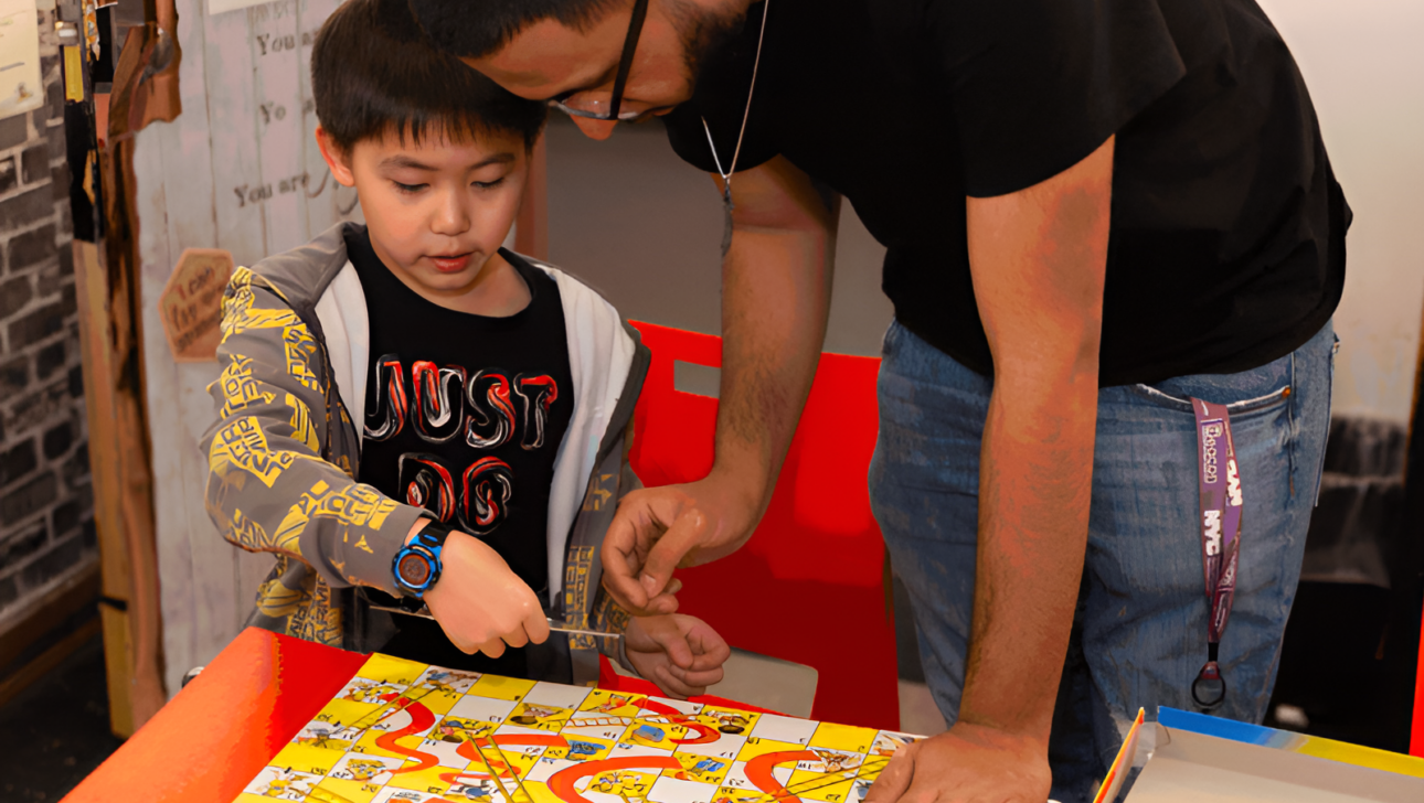 After school, a man leans over to help a child playing a Snakes and Ladders board game at Commonpoint, both concentrating on the game pieces in a room with varied decor.