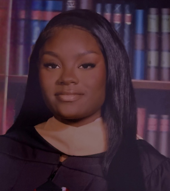 Roberta Gordon, dressed in graduation attire, poses confidently in front of a bookshelf backdrop.