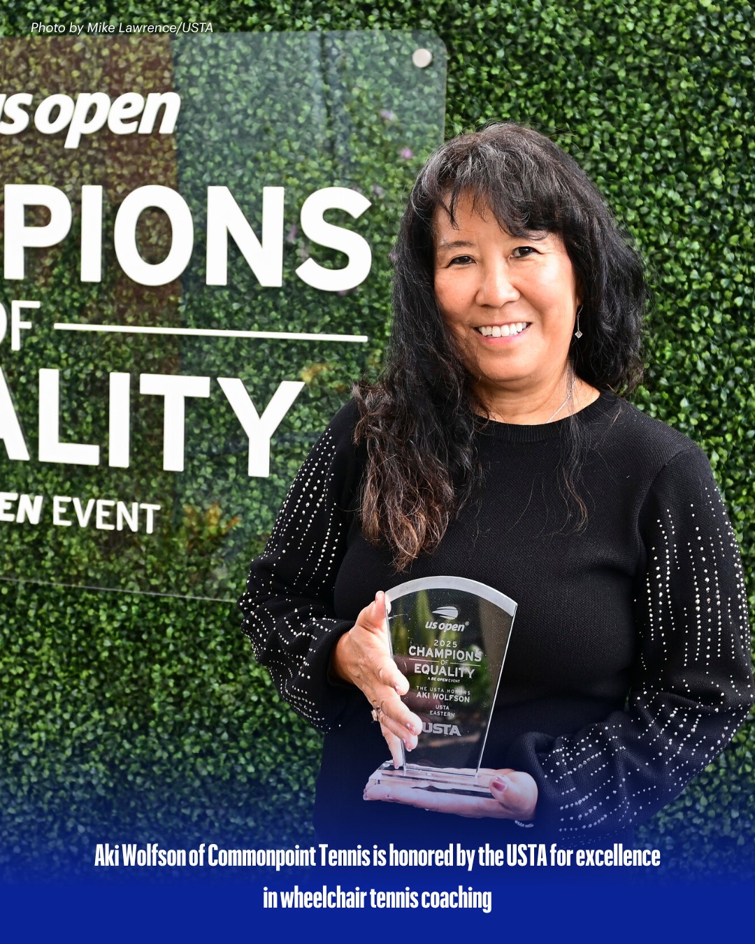 A woman smiles while holding a glass award in front of a "Champions of Equality" sign at a USTA US Open event, celebrating Aki Wolfson, Tennis Coach at Commonpoint.