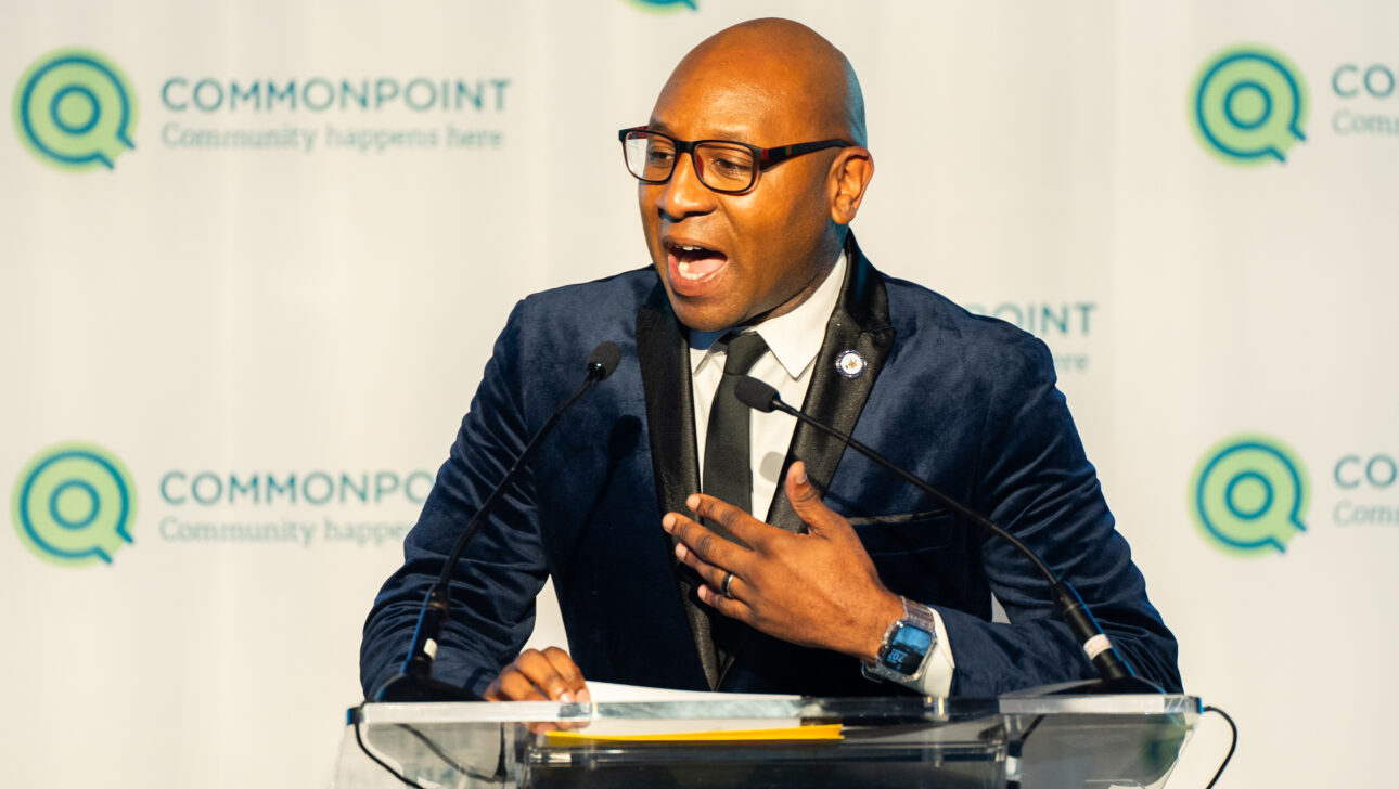 A man in a suit and glasses speaks at a podium during the Commonpoint Gala, with branded logos and the slogan "Community happens here" in the background.