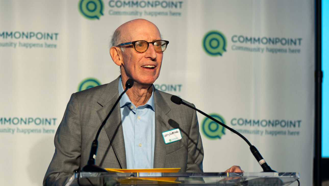 An older man in glasses and a suit speaks at a podium with microphones in front of a Commonpoint branded backdrop at the Commonpoint Gala.
