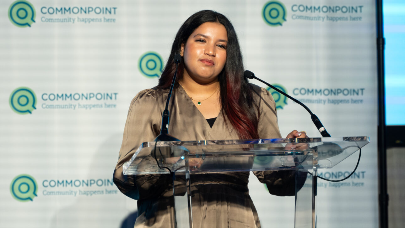 A woman stands at a clear podium speaking into microphones, with a Commonpoint Gala backdrop behind her.