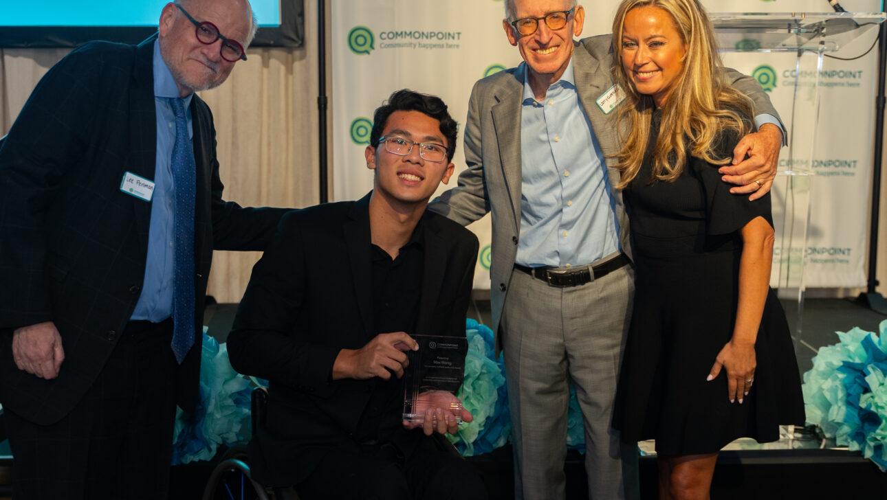 Four people pose and smile for a photo at the Commonpoint Gala; one person in a wheelchair proudly holds an award plaque.