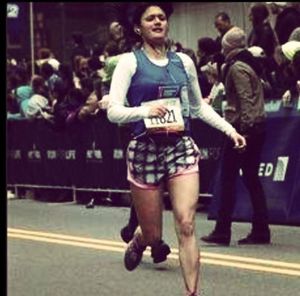 A runner in the TCS New York City Marathon approaches the finish line with a crowd of spectators watching from behind a barrier.