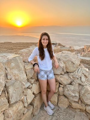 A woman in athletic wear stands by a stone wall, enjoying a scenic sunrise and expansive landscape, reminiscent of the inspiration found at the TCS New York City Marathon.