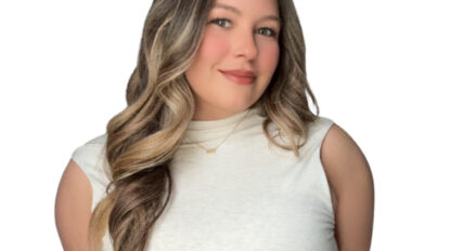 Woman with long wavy hair and a light sleeveless top poses against a white background, smiling slightly at the camera.