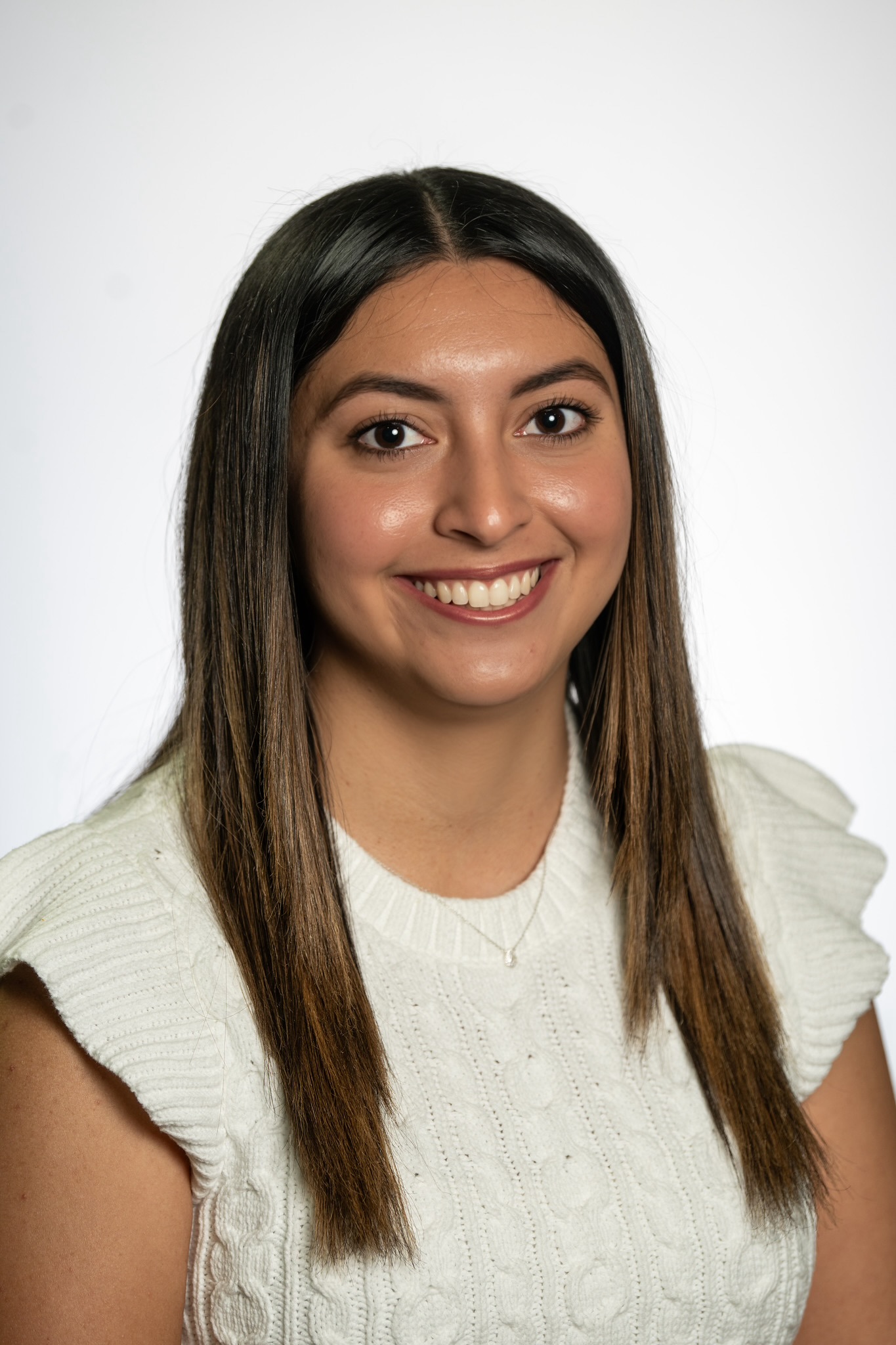 A woman with straight, dark hair wearing a white knit top smiles at the camera against a plain white background.
