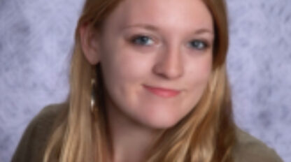Abby Parsons, a young woman with long blonde hair, wears a brown cardigan and floral top as she poses in front of a light gray textured backdrop.