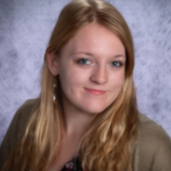 Abby Parsons, a young woman with long blonde hair, wears a brown cardigan and floral top as she poses in front of a light gray textured backdrop.