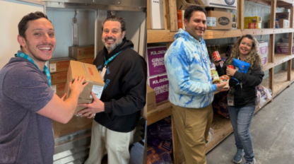 Two men place a box in a walk-in fridge during the Commonpoint Challenge, while a man and woman pose with food items on shelves in a storage area.